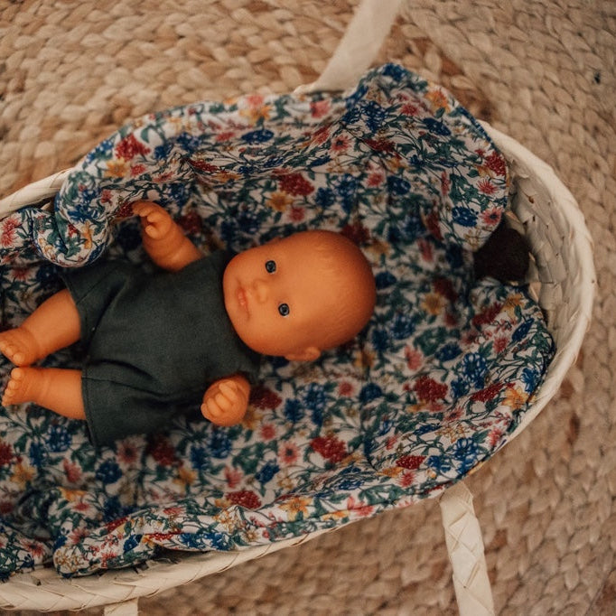 Baby doll in a floral blanket inside a woven basket on a textured surface